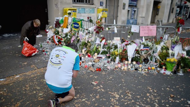 Members of the public view flowers and tributes on the pavement near the scene of Friday's Bataclan Theatre terrorist attack in Paris.