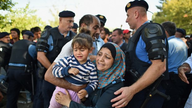 A migrant mother carries her daughter in her arms as she and other migrants force their way through police lines at Tovarnik station for a train to take them to Zagreb.