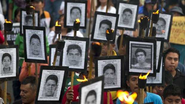 Family members of missing Mexican teachers and college students carry pictures of their loved one as they march with supporters on Tuesday.