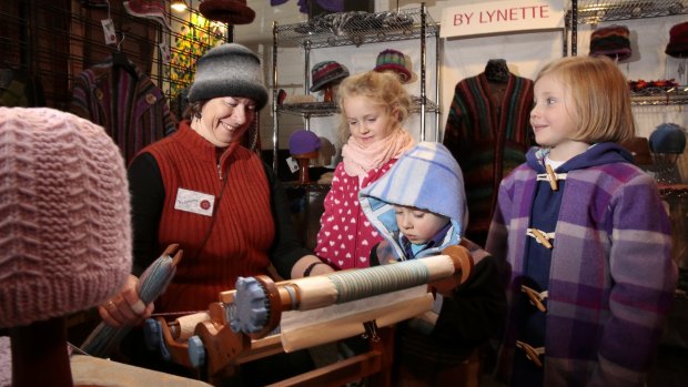 Lynette Swift, of Sydney, demonstrates weaving with a loom for Sienna Carloff, 6, of Murrumbateman, Aaron Jones, 4, and Sasha Jones, 6, of Cook, at the Handmade Markets at Exhibition Park in Canberra.   