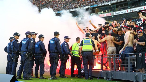 Wanderers fans in the crowd let off flares as police personnel look on.