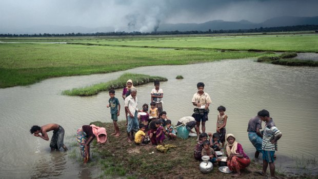 Rohingya refugees rest near the Naf River separating Myanmar and Bangladesh after crossing the border, as villages burns in the background.
