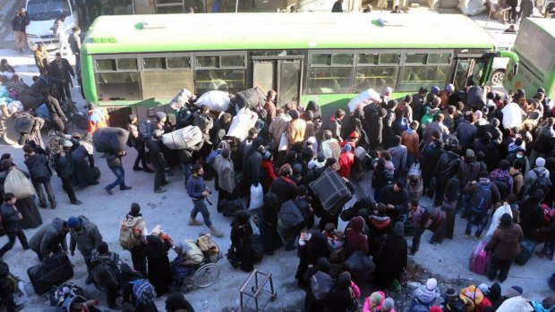 Residents gather near a green government bus as they hold their belongings for evacuation from eastern Aleppo, Syria.