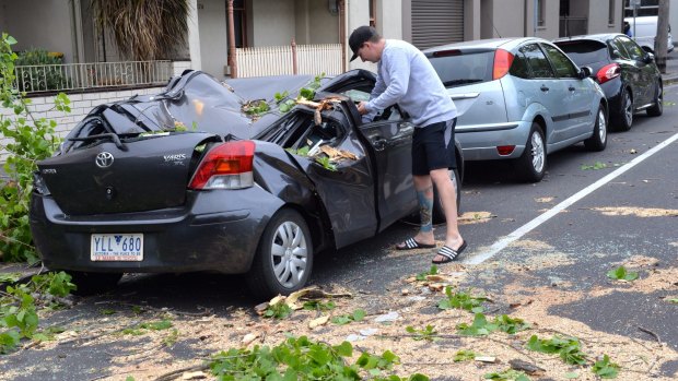 A man inspects a storm-damaged car in Carlton.