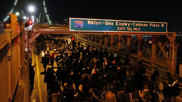 A group of protesters rallying against a grand jury's decision not to indict the police officer involved in the death of Eric Garner marches across the eastbound traffic lanes of the Brooklyn Bridge.
