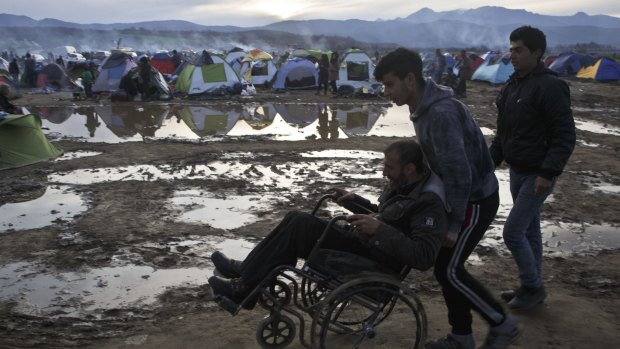 A migrant in a wheelchair is pushed across a flooded field at the northern Greek border station of Idomeni on Tuesday. 