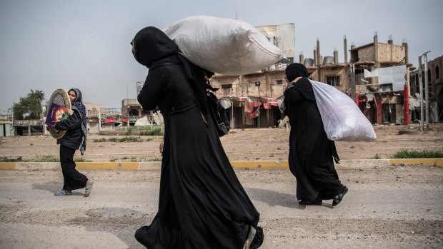 Displaced women carry possessions as they flee from their homes during fighting in west Mosul.