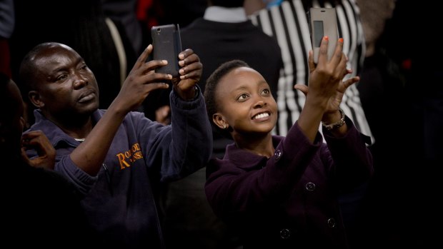 Members of the audience take selfies as President Barack Obama gives a speech behind them in Nairobi, Kenya.