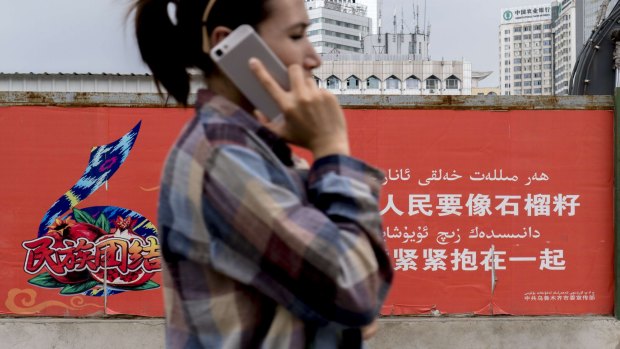 A Uygur woman walks past a propaganda sign in Urumqi, which reads: 'All different peoples should unite together just like pomegranate seeds."