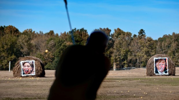 Jerry Wallace chips a golf ball towards targets with Hillary Clinton and Donald Trump's faces on them at a driving range in Texas.