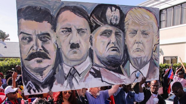 Haitian community members hold a sign depicting images of, from left, Joseph Stalin, Adolf Hitler, Benito Mussolini and Donald Trump during a protest near Trump's Mar-a-Lago estate on Monday.