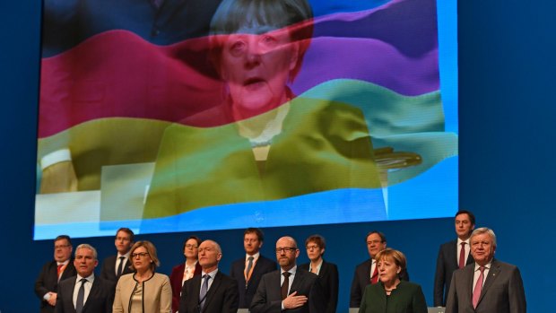 The CDU board sings the national anthem in front of a screen showing German chancellor Angela Merkel on the national flagon Wednesday.