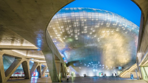 Dongdaemun Design Plaza - a Zaha Hadid-designed curving building of gleaming metal, lights up at night.