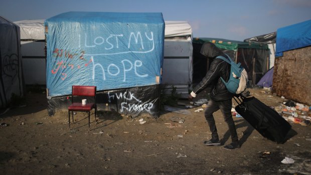 A migrant leaving the Jungle, Calais, walks past messages left on tents.
