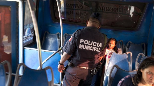 A girl riding a bus puts up her hands as a local policeman conducts a routine search at a checkpoint along the La Costera in Acapulco, Mexico. 