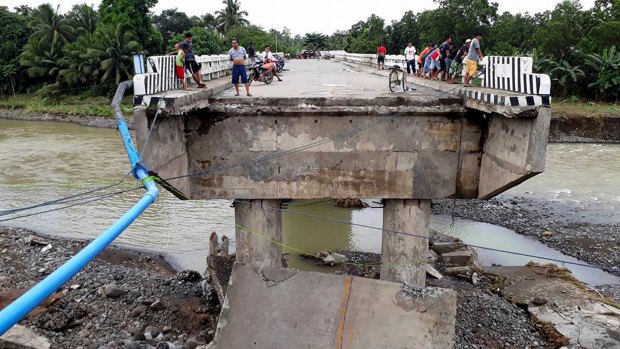 People gather on a bridge damaged by the onslaught of the flooding brought about by tropical storm Tembin.