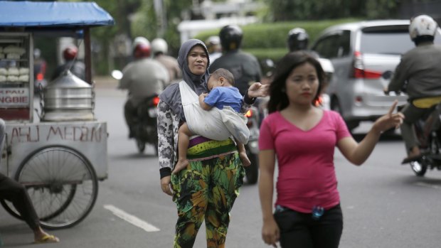 Yanti, carrying her child, and Fitri Andayani, in pink, offer their services as "jockeys" for Jakarta motorists.