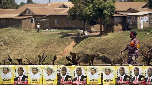 Pedestrians walk past campaign posters for long-time President Yoweri Museveni, as well as for local members of Parliament, in Kampala on Wednesday. 