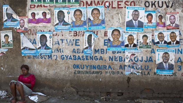 A woman sits against a wall plastered with campaign posters for opposition leader Kizza Besigye in Uganda's capital Kampala on Wednesday. 