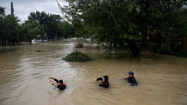 People wade through chest deep water down a street as a local reservoir nears capacity in Houston.
