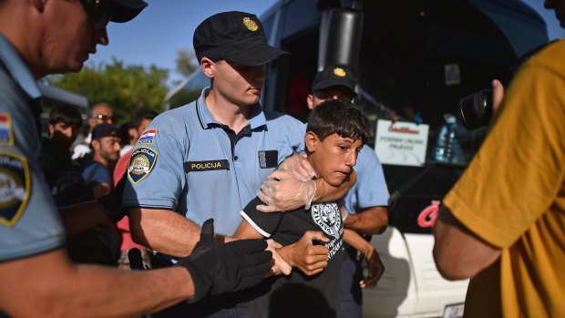 A young boy is held by police after trying to jump the queue as refugees board trains in Beli Manastir, Croatia, near the Hungarian border.