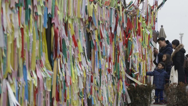A South Korean family reads messages on ribbons hanging on a wire fence wishing for the reunification of the two Koreas.
