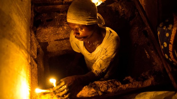 Dieusel Gerlin, a bayakou or waste cleaner, uses candles for light while descending into the pit of an outhouse, in Port-au-Prince, Haiti. Bayakou strip off their clothes and wrap themselves in rags to do a job so poor few admit to it.