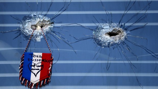 A French flag hangs from broken glass from a bullet hole in the window of the restaurant on Rue de Charonne, Paris, where attacks took place on Friday. 