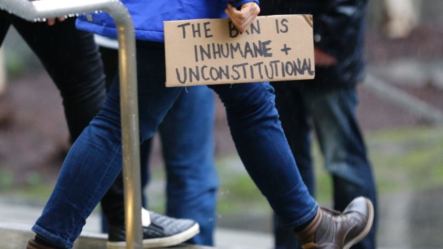 A person walks away from the federal courthouse in Seattle carrying a sign that reads "The Ban is Inhumane and Unconstitutional" on Friday.