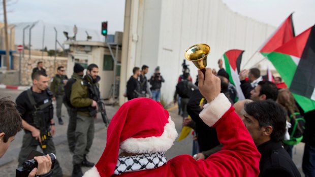 Palestinian protesters, some are dressed as Santa Claus, carry Palestinian flags and chant anti-Israel slogans in front of an Israeli checkpoint, in Bethlehem, West Bank, on Friday.