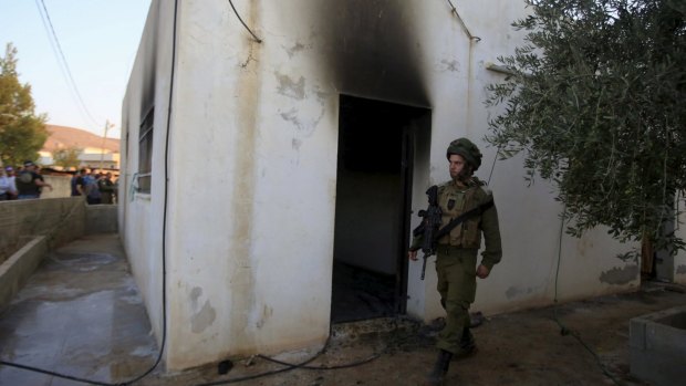 An Israeli soldier walks past the house torched in a suspected attack by Jewish Israeli extremists near Nablus on Friday.