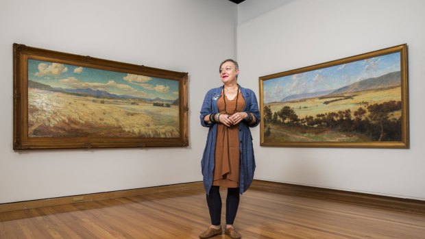 Curator Deborah Clark with two of the four paintings from 1913 of early Canberra. 
