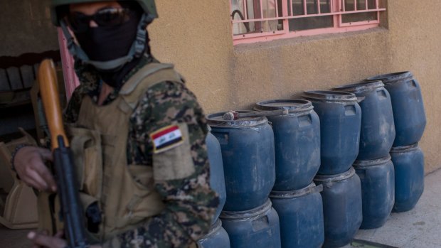 A NPU fighter is seen in front of drums of homemade explosive at a bomb making house used by IS.