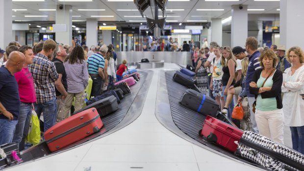 Travelers wait for their luggage from a conveyor belt.