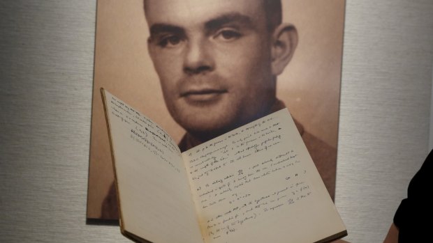 A notebook of British mathematician and pioneer in computer science Alan Turing in front of a photo of him at an auction preview.