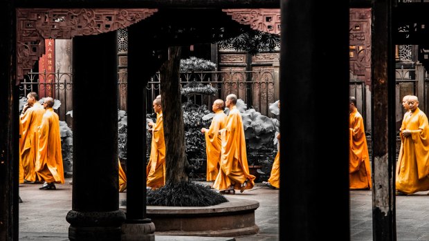 Buddhist monks in orange robes walks between columns of Wenshu Monastery in Chengdu, China.