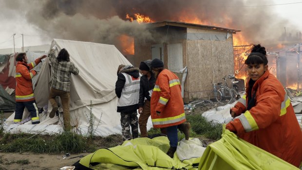 Charity workers pull tents away from burning shelters.