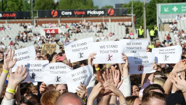 People in the One Love Manchester concert crowd hold placards reading "We Stand Together".