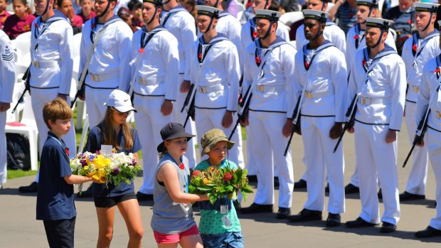 Children carry floral tributes to the Shrine on Friday as the Navy stands guard.