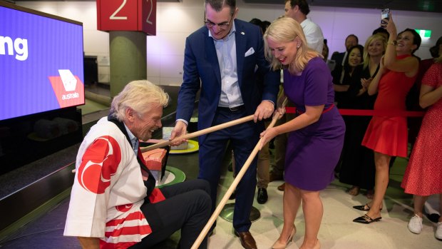 Virgin Australia CEO Paul Scurrah demonstrates how to dine at the 'giant sushi train' during a media event with Sir Richard Branson at Brisbane airport.