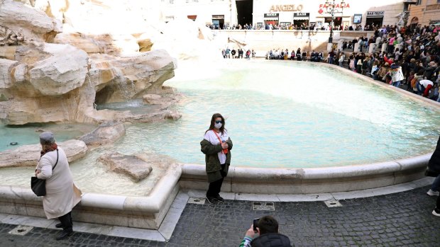 A tourrist wearing a protective face mask has a photograph taken at Trevi Fountain.