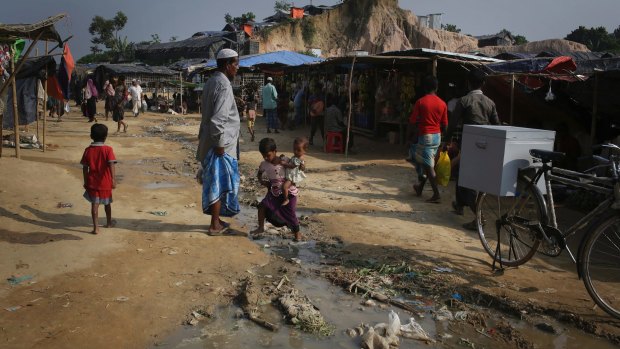 A Rohingya Muslim girl carries her baby sister as she walks across a stream of drainage water at the Thaingkhali refugee camp in Bangladesh.