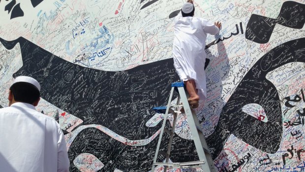 A boy writes a comment on a wall with a depiction of Qatar's emir, Sheikh Tamim bin Hamad Al Thani, that has attracted signatures and comments of support from residents, amid the diplomatic crisis.