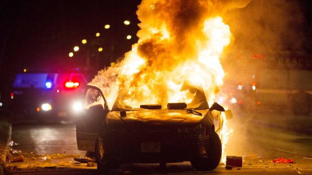 A car burns as a crowd of more than 100 people gathers following the fatal shooting of a man in Milwaukee.