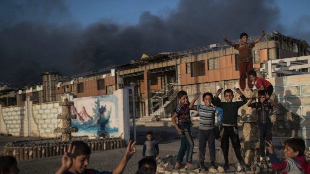 Children pose playfully as smoke rises from burning oil fields in Qayara, some 50 kilometres south of Mosul.