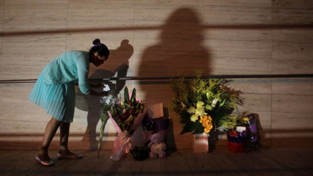 A young girl leaves flowers at the front of NSW Police Headquarters in memory of police employee Curtis Cheng.