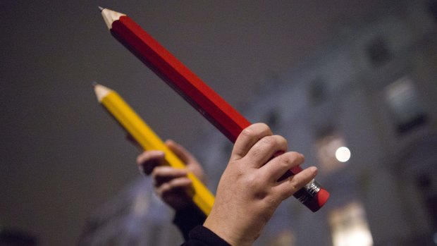 People hold up giant pencils at a vigil outside The French Institute in London on Friday.