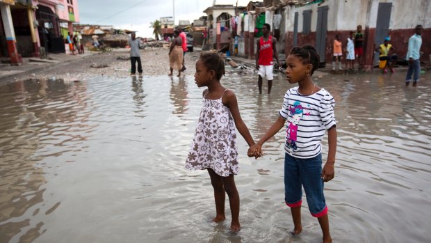 Girls hold hands as they help each other wade through a flooded street after the passing of Hurricane Matthew in Les Cayes, Haiti.