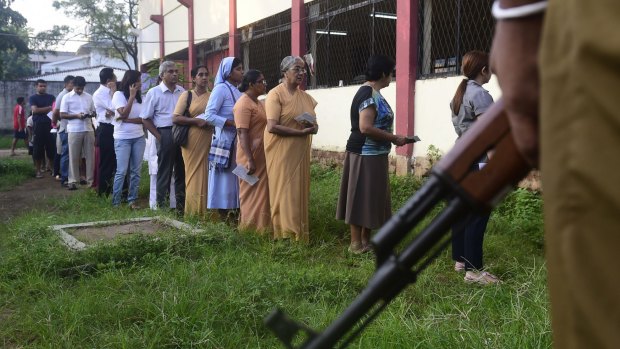 People queue to vote as police stand guard in Colombo.