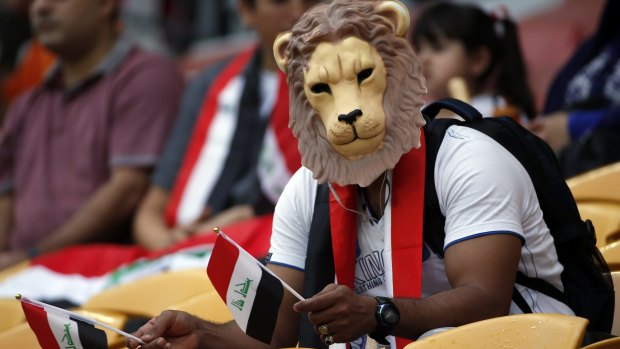 An Iraqi supporter sports a lion's mask and holds flags in both hands as he urges his team on.
